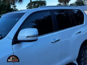 A technician carefully applying a dark tint film to the side window of a luxury vehicle.