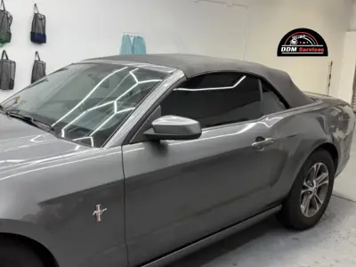Side view of a grey Ford Mustang convertible with dark tinted windows inside a professional detailing shop.