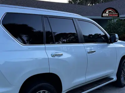 A technician carefully applying a dark tint film to the side window of a luxury vehicle.