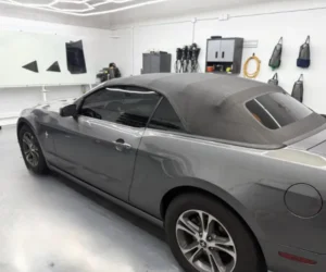 A professional applying a protective film layer to the glossy white exterior of a vehicle.