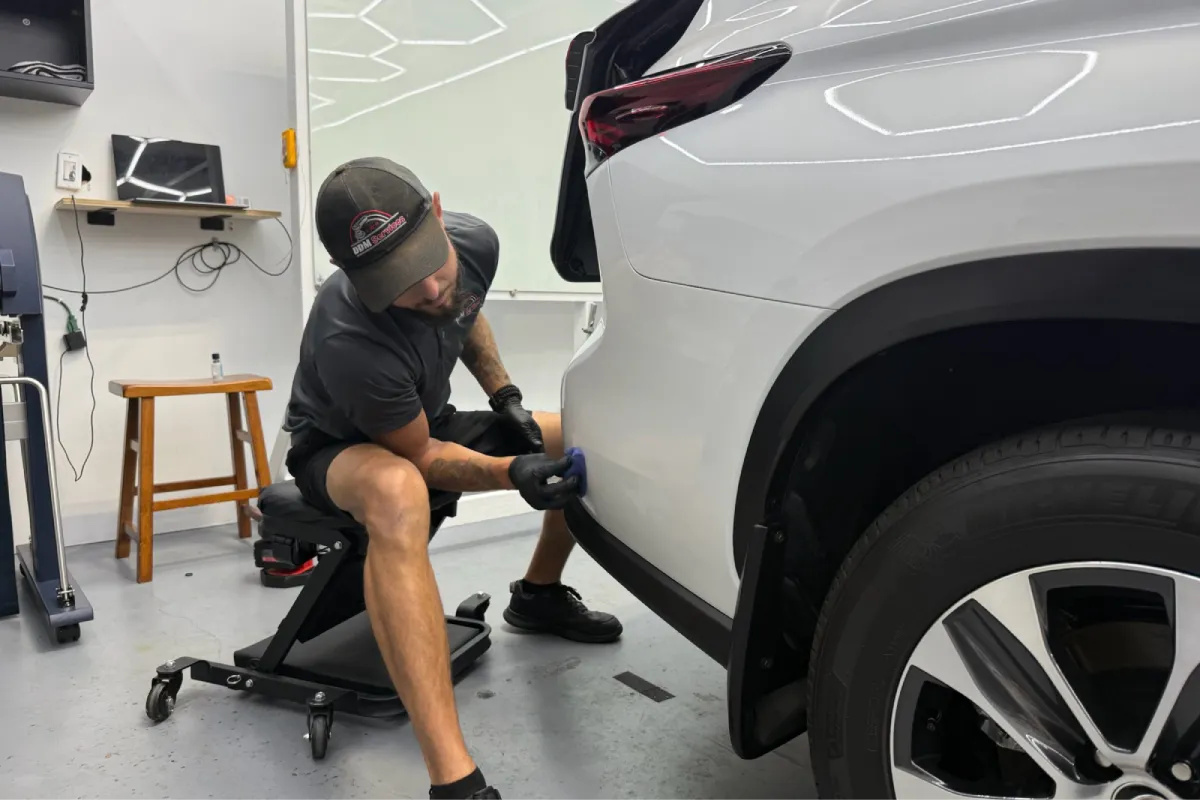 Technician working on the side of a white vehicle, performing paint correction.